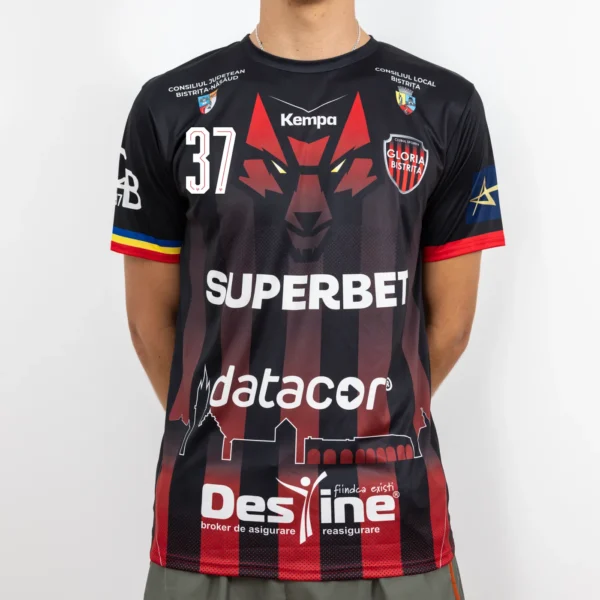 Tricou de joc handbal Gloria Bistrița – Negru (față) Tricou de joc handbal Gloria Bistrița, negru cu accente roșii, văzut din față — sigla Kempa, stema clubului și sponsorii